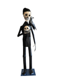 A papier-mâché skeleton figurine wearing a black suit and holding a skull with a black raven on its shoulder.