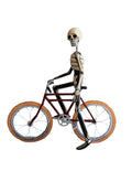 A papier-mâché skeleton figurine posed riding a vintage-style bicycle.