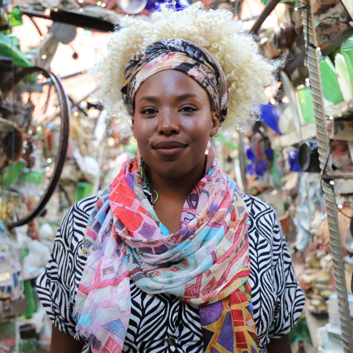 A smiling woman in a mosaicked hallway wearing a mosaicked light-weight scarf.