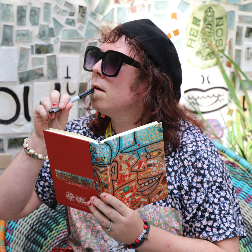 A woman poses with a sketchbook that has a mosaic image on the front