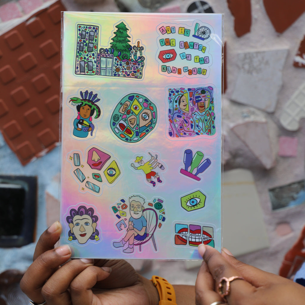 Hands hold a sheet of colorful stickers inspired by Philadelphia's Magic Gardens. The stickers are on a holographic silver background. 