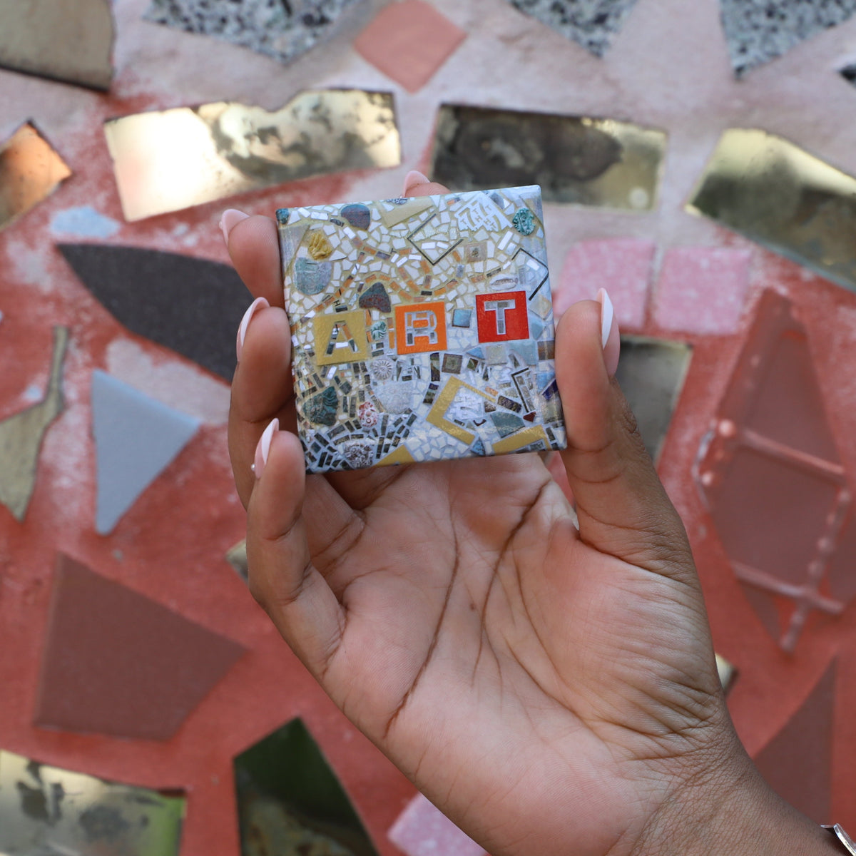 A square refrigerator magnet with a photo of a mosaic on it containing the word "art."