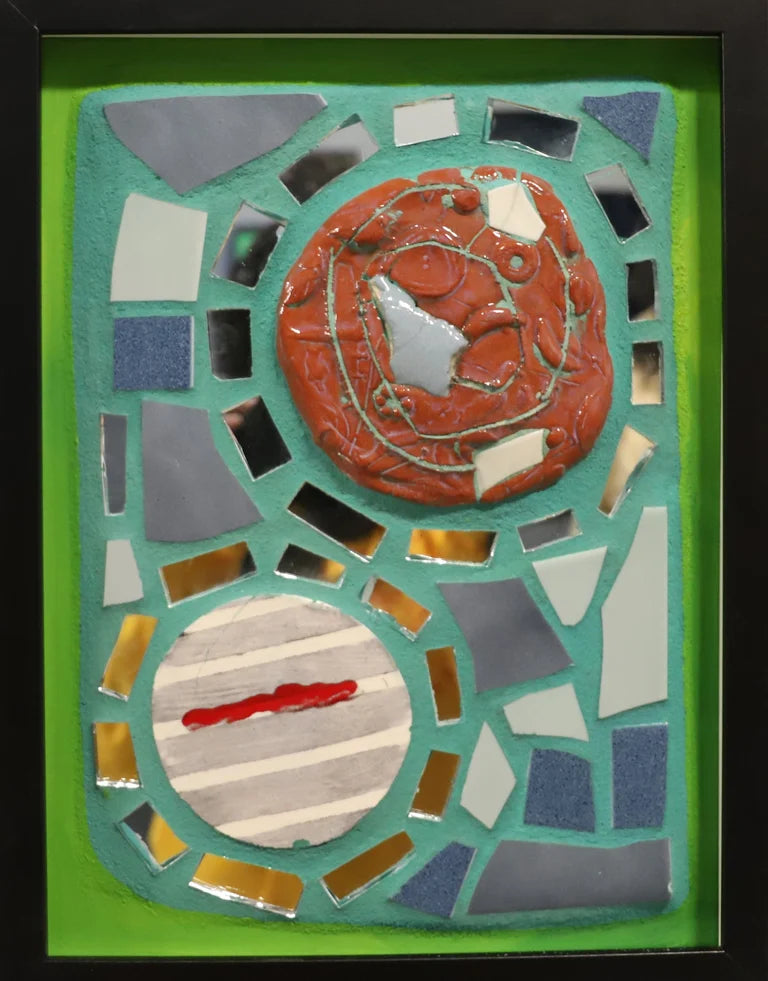 Framed mosaic feature two round tiles surrounded by mirror and other tiles on blue grout with a green border.