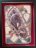 Framed mosaic featuring the mold of a foot against pink grout and a red border.