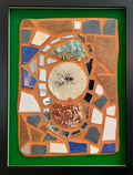 Framed mosaic with colorful tiles and mirror pieces on orange grout with a green border.