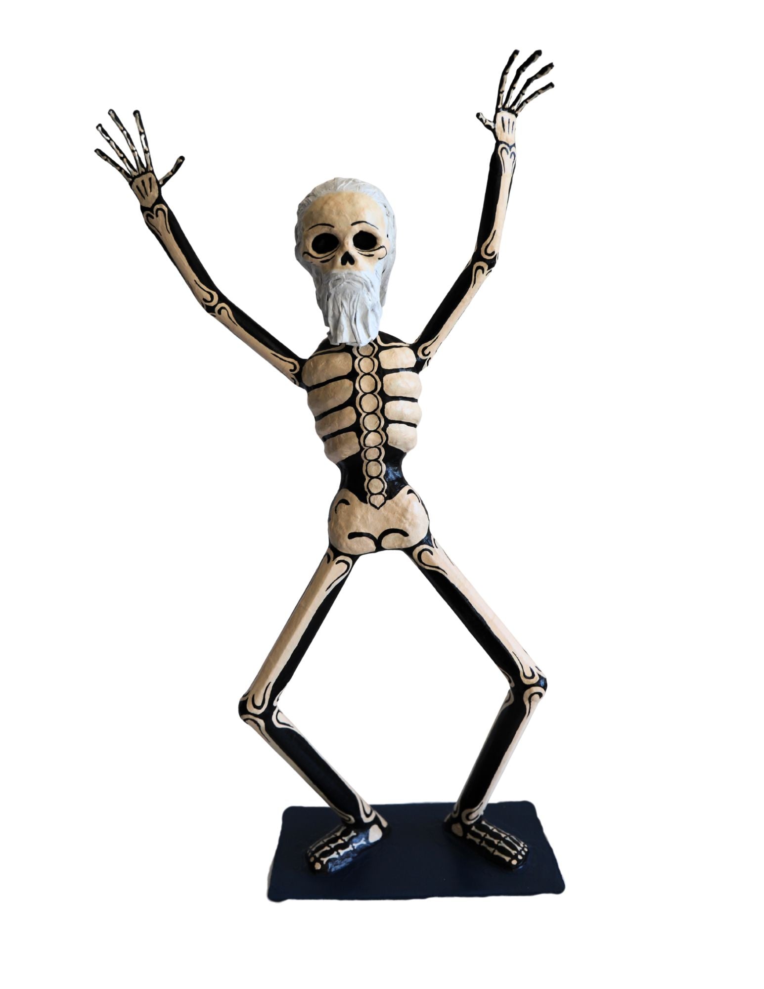 A papier-mâché skeleton figurine with raised arms, featuring beige bones with black joints and a white beard.